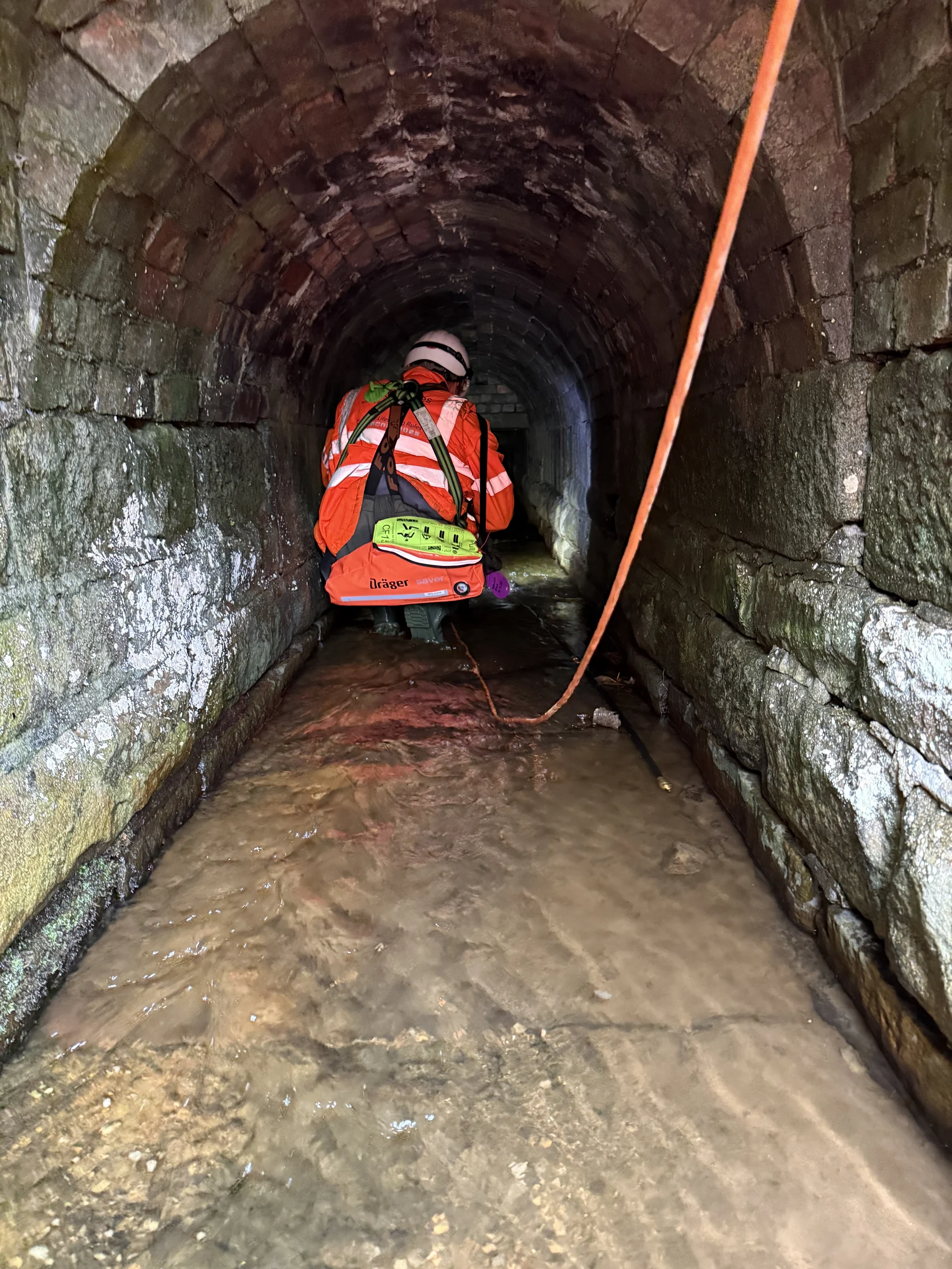 Confined-space operative progressing through a masonry culvert